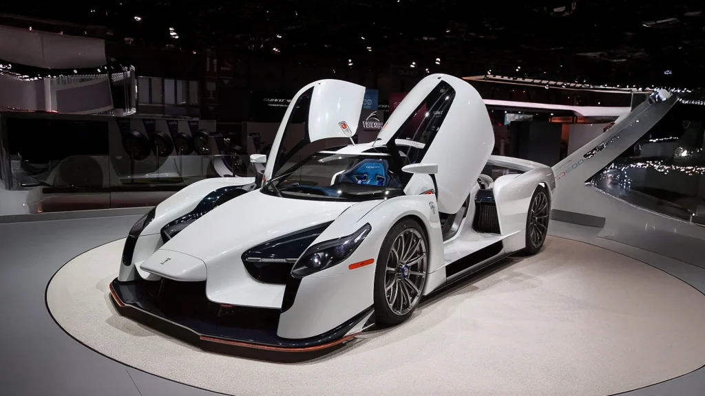 SCG003S with open butterfly doors displayed on a raised platform at an auto show, highlighting its aerodynamic design and bespoke craftsmanship